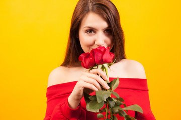 Cheerful young beautiful woman holding a red rose and looking a the camera over yellow background