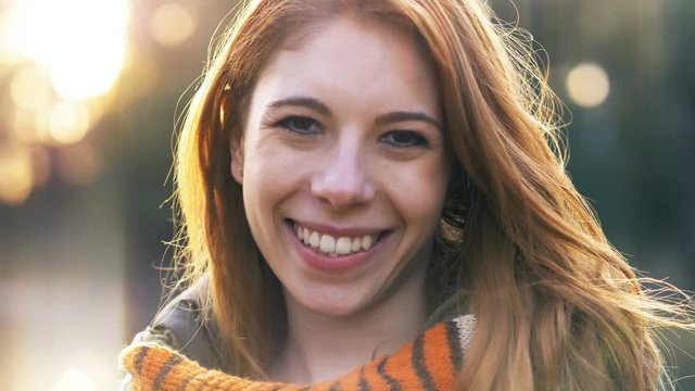 Beautiful happy red haired young woman smiling at camera in the park