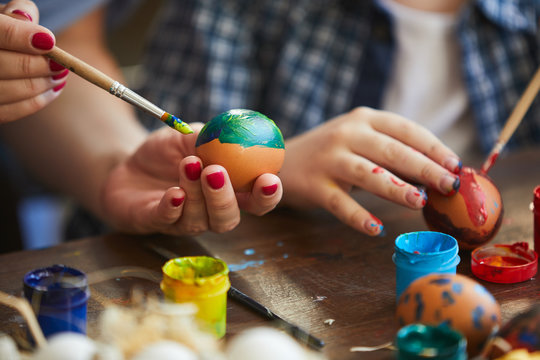 Closeup of child painting Easter eggs with mother, copy space