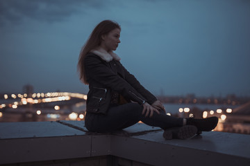 Silhouette of alone woman sitting on the roof, city on background