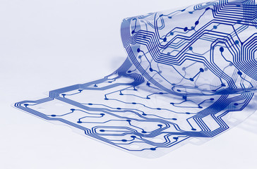 Electronic flex circuit board. Clear membrane of dismantled computer keyboard. Silicone sheet. PCB detail curled to a roll. Artistic design. Abstract bent plastic film. Blue pattern. White background.