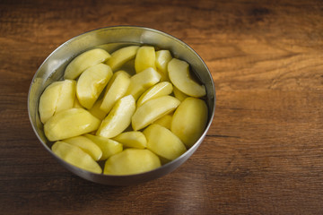 Cut pieces of apple in a bowl with water on wooden table top.	