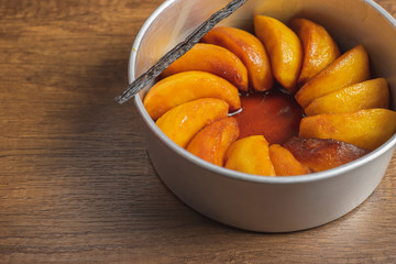 Cooked apple pieces with caramel arrange in a metal cake tin on wood table top.	