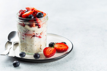 Overnight oats with chia seeds and fresh strawberries and blueberries in a glass jar. Healthy breakfast.
