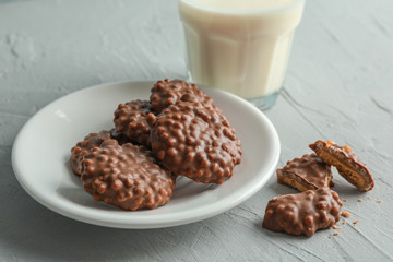Glass of milk and plate with chocolate cookies on grey table