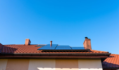 Solar panel on the red house roof in the background of blue sky.
