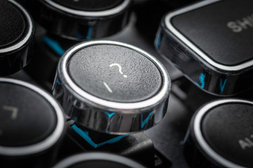 An extreme close-up or macro shot of a round slash and question mark symbols key on a vintage-inspired retro-style clicky black-and-silver metal typewriter keyboard.