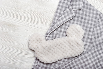 Flat lay from sleeping clothes, warm soft pajamas and fluffy mask with ears on white wooden background with copy space. Top view.