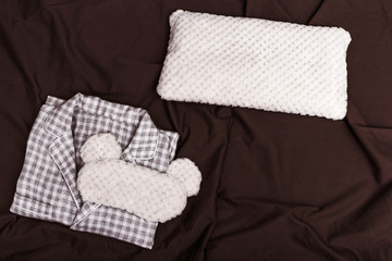 Checkered warm Pajamas for Womens, soft cushion and eye mask for sleeping on dark sheet on bed. Top view. Flat lay.