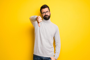 Man with beard and turtleneck showing thumb down sign with negative expression © luismolinero