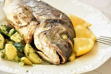 dorado baked fish in the oven, lies with potatoes and lemon on a white plate