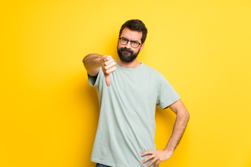 Man with beard and green shirt showing thumb down sign with negative expression © luismolinero