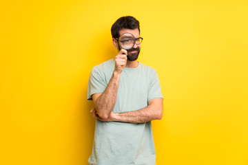 Man with beard and green shirt taking a magnifying glass and looking through it