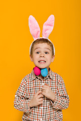 Portrait of cute little child boy with Easter bunny ears holding colorful eggs on yellow background. Happy easter