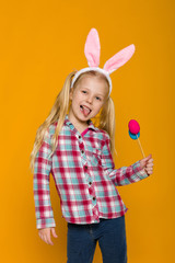 Portrait of funny little child girl with Easter bunny ears holding colorful eggs on yellow background. Happy easter