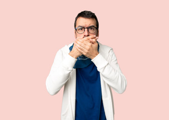 Handsome man with glasses covering mouth with hands for saying something inappropriate on isolated pink background