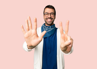 Handsome man with glasses counting seven with fingers on isolated pink background