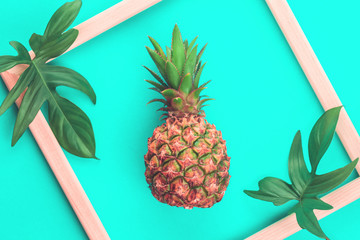 Baby pineapple with wooden frame and leaves on trendy mint background. Flat lay exotic summer concept with copy space