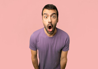 Handsome man with surprise and shocked facial expression on isolated pink background