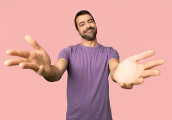 Handsome man presenting and inviting to come with hand on isolated pink background