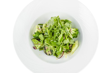 Salad of green vegetables with broccoli, zucchini and walnut dressing on a plate on a white background, top view isolated
