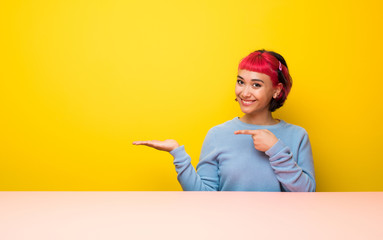 Young woman with pink hair holding copyspace imaginary on the palm to insert an ad
