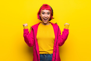 Fototapeta premium Young woman with pink hair over yellow wall celebrating a victory in winner position
