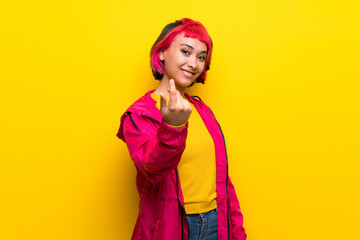 Young woman with pink hair over yellow wall inviting to come with hand. Happy that you came