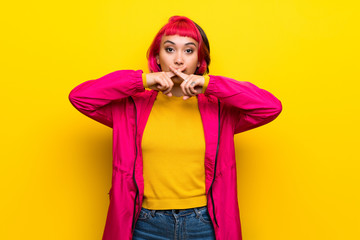 Young woman with pink hair over yellow wall showing a sign of silence gesture