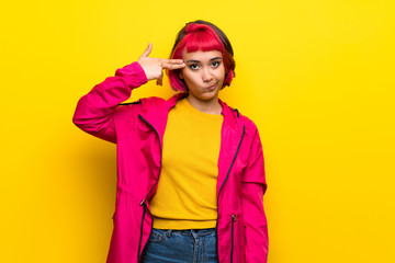 Young woman with pink hair over yellow wall with problems making suicide gesture