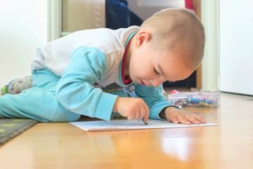 Cute little kid boy drawing a story with colorful pens at home.