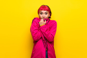 Young woman with pink hair over yellow wall freezing
