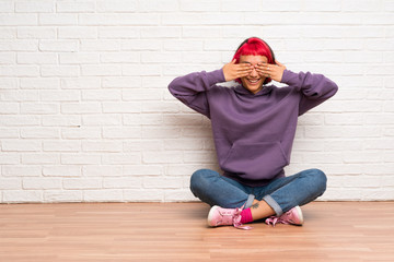 Young woman with pink hair sitting on the floor covering eyes by hands