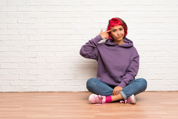 Young woman with pink hair sitting on the floor making the gesture of madness putting finger on the head