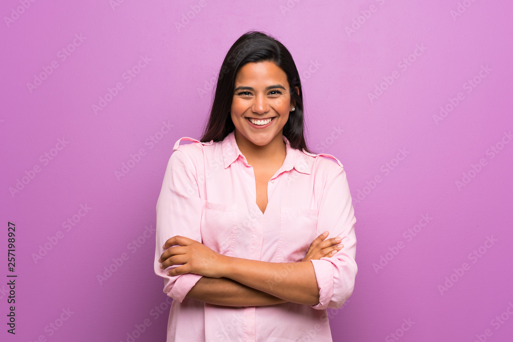 Wall mural Young Colombian girl over purple wall keeping the arms crossed in frontal position