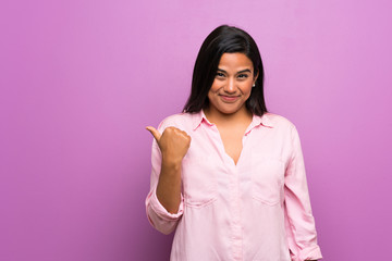 Young Colombian girl over purple wall pointing to the side to present a product