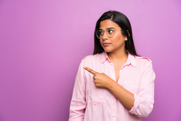 Fototapeta premium Young Colombian girl over purple wall pointing finger to the side