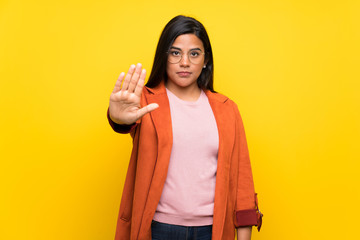 Young Colombian girl over yellow wall making stop gesture denying a situation that thinks wrong