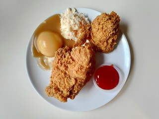 Fried chicken serve with chicken,coleslaw,mashed potato with gravy sauce and chili sauce on white plate.