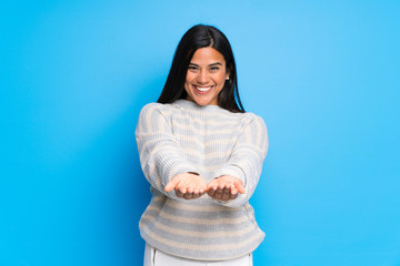 Young Colombian girl with sweater holding copyspace imaginary on the palm to insert an ad