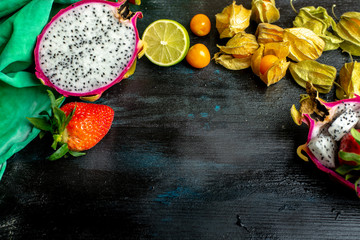 pink and white dragon fruit surrounded by fresh strawberries and physalis