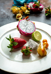pink and white dragon fruit surrounded by fresh strawberries and physalis