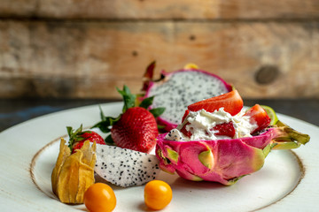 on a white, wooden plate, lie the fresh fruit of strawberries, among them a beautiful, pink dragon...