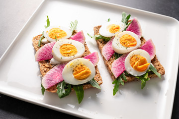Colorful sandwiches of cereal bread with boiled eggs with radish and arugula