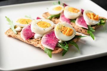 Colorful sandwiches of cereal bread with boiled eggs with radish and arugula