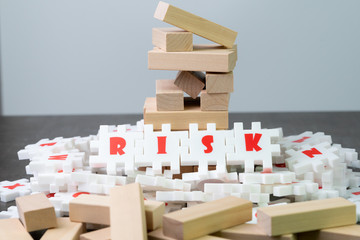 Risk management concept, white puzzle jigsaw with alphabet building the word Risk at the center of dark chalkboard with collapse wooden tower game