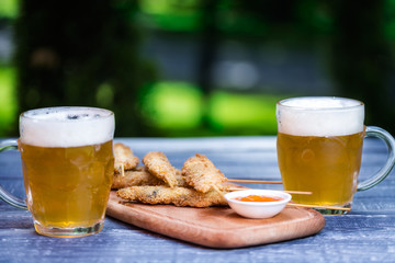 Beer snacks set. Chicken wings on sticks and two mugs of beer. On the cutting board and green summer background