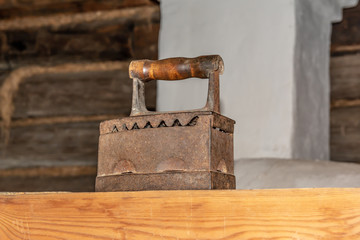 Old large iron is in a wooden house on the stove next to the pipe