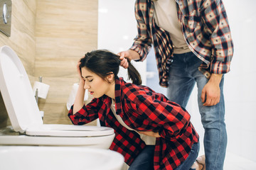 Sad woman throwing up in the toilet, hangover