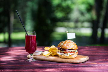 The perfect meat burger with crisps and fresh cold lemonade. On the cutting board, and green summer background.